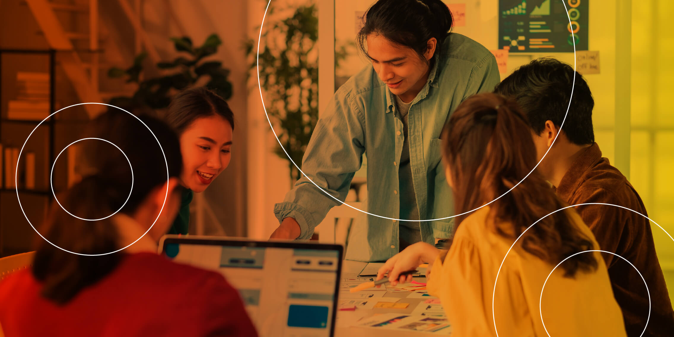 Group of people engaged in a lively brainstorming session around a table with notes and laptops.